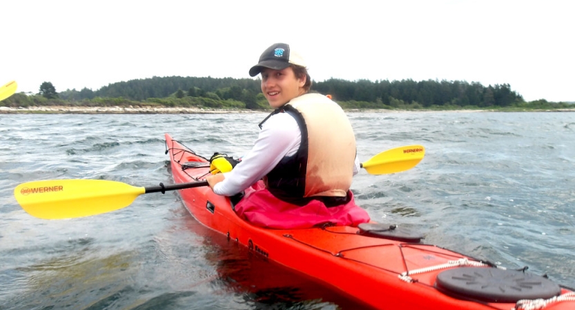 A person wearing a life jackets smiles while paddling a red kayak